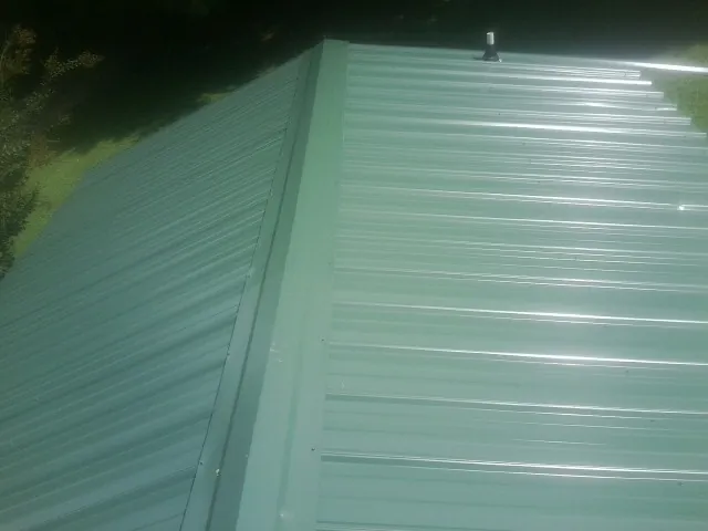 New green metal panels meeting at the ridge of a roof — Flat Roof Repair work by our crew in Medway