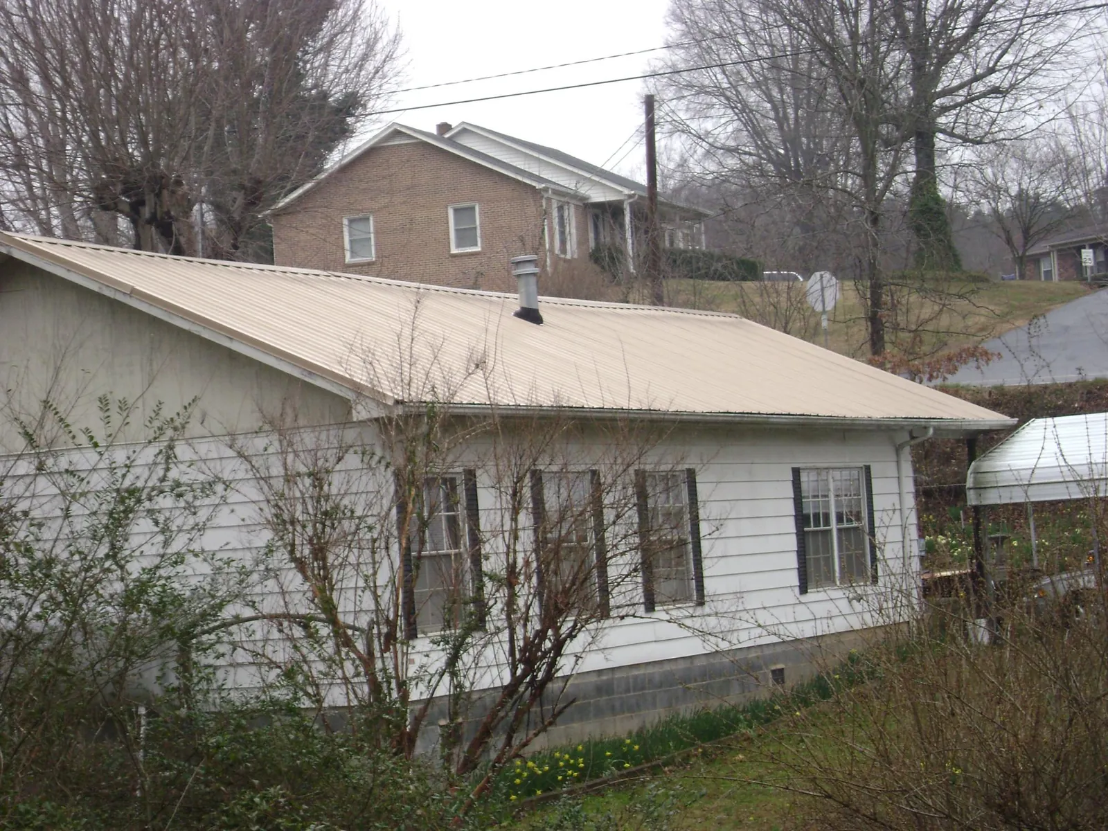 Tan metal roof on a white sided house set into a hillside — Commercial Roofing by Roofing Brothers in Medway